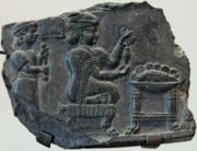 Relief of a woman being fanned by an attendant while she holds what may be a spinning device before a table with a bowl containing a whole fish