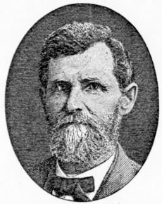 A middle-aged man with a graying beard is wearing a bow tie and suit jacket