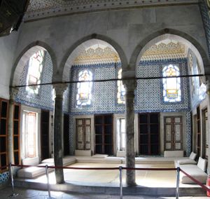 salle décorée de carrelage bleu ; trois arches ; des divans au sol