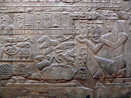 Relief of an ornately dressed man kneeling and holding a tray of food and flowers