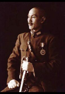 A Chinese man in military uniform, smiling and looking towards the left. He holds a sword in his left hand and has a medal in the shape of a sun on his chest.