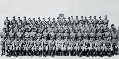 A formative black-and-white photograph of military personnel. The men wear khaki shirts and shorts with long, dark-coloured socks. They all wear dark berets.