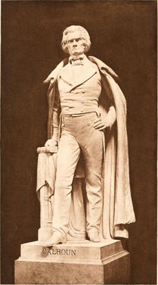 Life-sized statue, standing with full cloak to ankles, left hand on hip, right hand on book, serious and distinguished demeanor