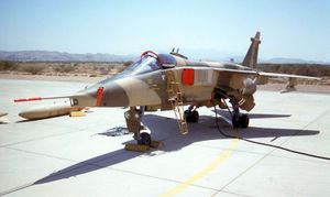 A Jaguar in desert camouflage scheme parked on hardstanding. The cockpit canopy is just open, with covers on the air intakes and on the nose probe, and a ladder giving access to the cockpit