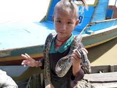 Boy on a boat holding a tame python about his neck.