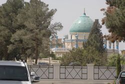 A color photograph of a blue and white mosque nestled behind trees