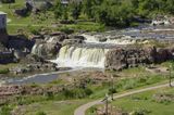 A wide waterfall plunges over rock ledges amid green fields