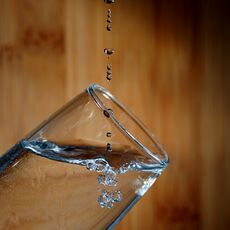 Water dripping into a glass, showing drops and bubbles.