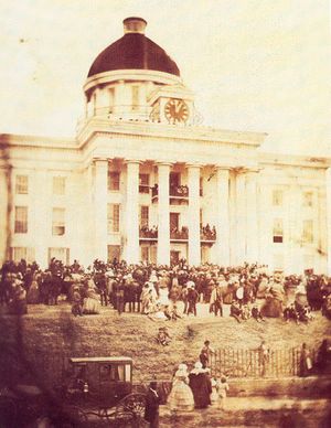 building with dome, clock and columns in background, crowd in midground, street and carriage in foreground