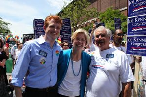 Two older men and an older woman stand in a crowd with signs reading "Joe Kennedy for Congress".